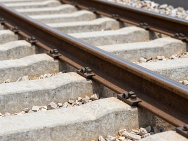 Macro shot of steel railway tracks and concrete sleepers under bright daylight, sharp focus, technical angle