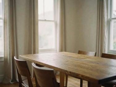 A sun-drenched living room with a heavy oak dining table, soft linen drapes, warm editorial photography, natural afternoon window light, muted earthy tones, medium format film, soft shadows