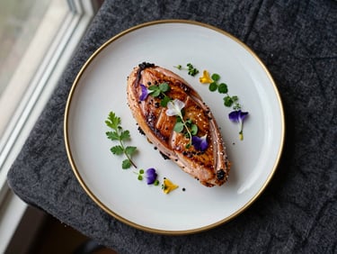 Overhead study of a single finished dinner plate — seared duck breast with a petal-scattered herb garnish, gold rim plate on dark linen, a small botanical sprig beside it — diffused natural window light from the left