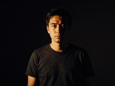 Low-key dramatic portrait of a film director in a dark studio, warm tungsten side-light, deep shadows, 35mm grain