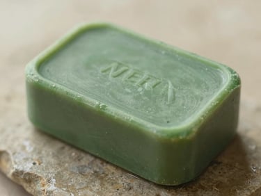 Close-up of a green clay soap bar resting on a wet stone, macro texture, soft morning light