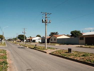 Loteamento urbano aberto com postes de energia instalados, meio-fio pronto e pavimentação asfáltica limpa sob céu azul