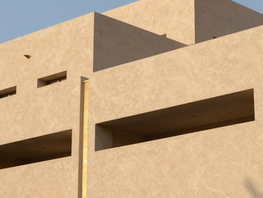 Close-up of clean architectural textures, smooth plaster and sand-gold metallic accents on a modern building exterior under soft golden hour light, 35mm lens