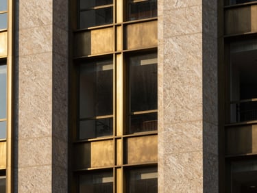 Extreme close-up of travertine stone and brushed brass architectural details on a modern skyscraper facade, high-contrast afternoon sun