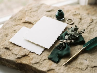 A clean mockup of high-end business stationery on textured sandstone, soft natural daylight, deep forest green accents, shallow depth of field