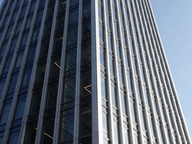 Premium architectural photography of a modern glass and steel corporate tower facade, sharp architectural angles, high-contrast bright sunlight, deep navy tones, editorial style