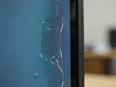 Extreme macro close-up of a cracked television LCD panel edge under cool workshop lighting, fractured pixel lines visible, sharp technical detail, no people