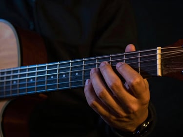 Close-up of fingers pressing guitar frets, electric blue rim lighting, dark studio