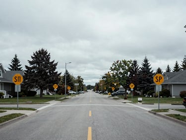 Wide shot of a suburban street intersection with visible stop signs and speed limit signs, overcast Canadian daylight, no people