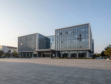 A wide, low-sun morning view of a modern civic administration building with clean geometric glass lines and a wide open plaza.