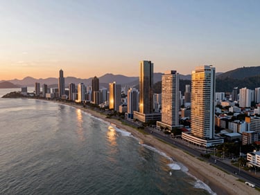 Wide panoramic drone shot of Balneário Camboriú coastline during golden hour sunset, soft warm light reflecting off modern architectural towers and the calm sea, negative space on the left.