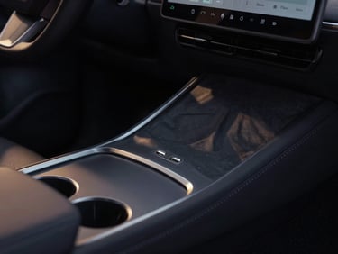 Close-up detail of a modern sleek electric car rear console, individual climate control screen glowing softly, USB ports, clean minimalist design.