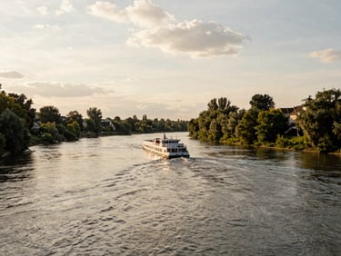 A scenic river bend in Europe with a slow-moving cruise vessel in the distance, warm overcast daylight, peaceful and relaxing composition.