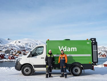 Wide environmental shot of two property maintenance workers standing next to a clean service vehicle in Vadsø, snowy mountains in the far background, crisp Arctic daylight, 35mm