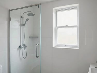 Bright bathroom with white tiles, frameless glass shower, brushed chrome fixtures, natural light from frosted window