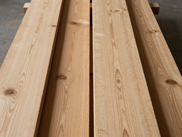 Close overhead shot of softwood and hardwood timber planks laid side by side on a factory floor, grain patterns and density differences visible under tungsten light, no people