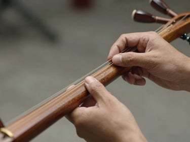 Close-up of hands tuning a dotara instrument in natural daylight, worn wood of the neck visible, soft interior light, no posed elements