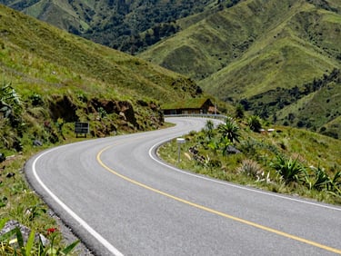 Bright daylight shot of a clean, newly paved mountain road winding through lush green hills in Yauco.