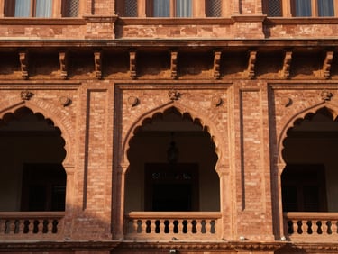 Architectural detail of an elegant heritage hotel facade in Lahore, warm brickwork, classical arches, soft morning light, 35mm photography