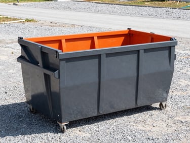 Wide-angle shot of a 20-yard roll-off dumpster at a home renovation site, crisp daylight, high-contrast gravel background.