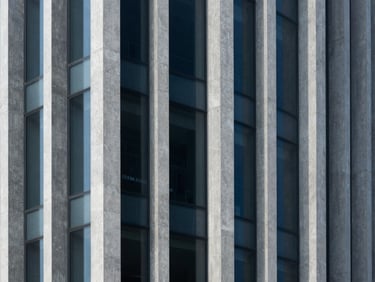 Abstract architectural geometry of a modern concrete and glass building facade, clean vertical lines, deep shadows, cool blue and slate tones.