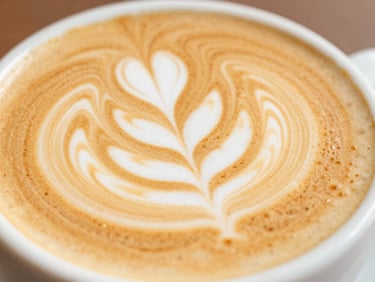 Close-up macro shot of a freshly poured latte with detailed leaf latte art in a ceramic cup, warm morning light, shallow depth of field