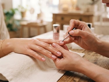 Macro close-up of hands applying delicate nail polish in a warm-lit boutique salon, soft pink and cream tones, shallow depth of field, 35mm