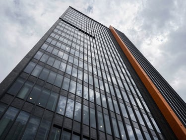 Wide-angle architectural view of a modern steel skyscraper facade reflecting high-contrast overcast clouds.