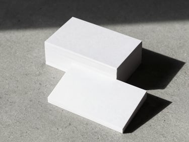 Tactile corporate stationery. A stack of thick, textured white paper business cards casting a sharp shadow on a grey concrete desk, neutral studio light.