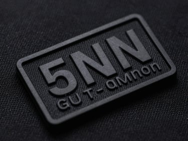 Tactile macro photography, sharp directional lighting, close-up of a molded PVC tactical patch with raised 3D lettering on a textured black background.
