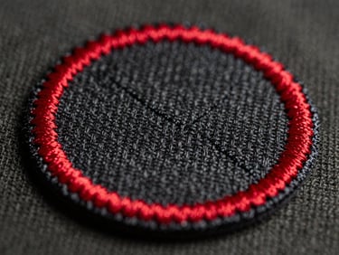 Tactile macro photography, hard side-lighting, extreme close-up of a classic embroidered military patch with a thick red merrowed border on dark canvas.