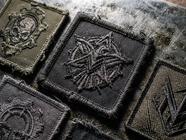 Tactile macro photography of custom patches on a steel plate, hard directional side-lighting, extreme close-up showing thick merrowed borders and heavy thread textures.