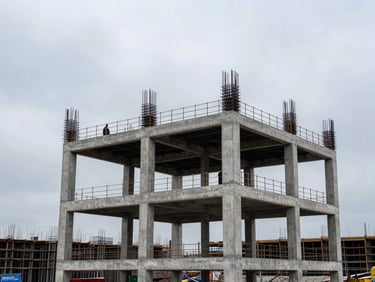 Wide environmental shot of a reinforced concrete frame mid-pour, formwork still in place, workers visible at upper level against an overcast sky, structural scale dominating the frame, cool grey daylight, no faces legible