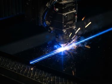 Macro close-up of a laser head emitting a precise electric blue beam cutting through a sheet of dark acrylic, sharp industrial photography, high-contrast dark studio lighting, crisp depth of field, dark background.