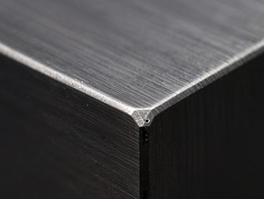 Macro close-up of a laser-cut edge on stainless steel, showing a clean, burr-free finish, high-contrast dark studio lighting, crisp depth of field.