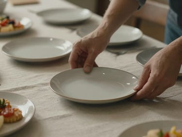 Close-up of hands carefully arranging simple, respectful food platters on a plain linen tablecloth, muted warm light, quiet and orderly composition