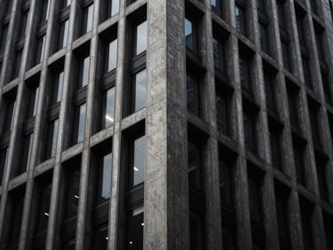 Moody architectural photography of a modern concrete and steel skyscraper facade, low-key dramatic lighting, deep charcoal and brushed silver tones, high contrast, 35mm
