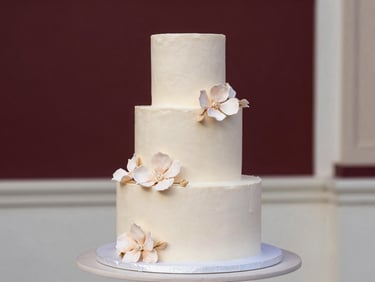 A stunning, minimalist tiered wedding cake decorated with delicate handmade sugar flowers on a clean pastel pedestal, soft natural light
