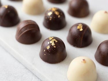 Macro shot of artisanal chocolate truffles and gourmet bombons with gold leaf detailing, arranged on a clean marble slab, soft lighting, editorial style