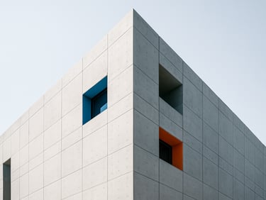 Wide-angle architectural photograph of a minimalist concrete skyscraper facade against a stark white sky, casting sharp geometric shadows, high-key natural daylight, 35mm.