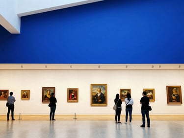 Wide environmental photo of a bright modern museum gallery with visitors looking at paintings on a sunny day