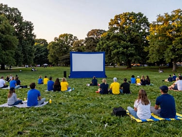 Outdoor movie screening in a green public park at sunset with families sitting on blankets, inviting atmosphere