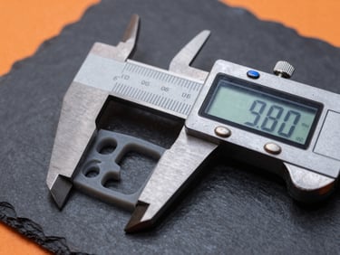 Close-up of a digital caliper measuring the precise millimeter thickness of a printed gray polymer prototype under high-contrast studio lighting