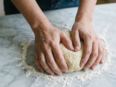 Overhead macro shot of hands kneading rustic dough on a flour-dusted marble counter, soft Scandinavian daylight, shallow depth of field