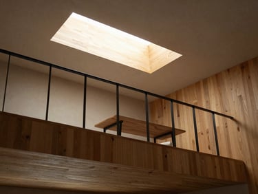 Looking up at a modern timber-clad mezzanine level with black steel railings, warm light from an overhead skylight, minimalist desk visible.