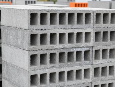 Neatly stacked hollow concrete blocks in an outdoor yard, showing the hollow core geometry, crisp daylight, 35mm