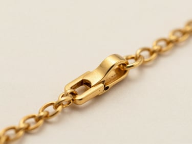 Extreme macro closeup of a gold necklace clasp resting on a neutral warm-white surface, soft diffused studio strobe from upper left revealing the precise hand-filed joint and textured link detail, shallow depth of field isolating the metalwork against a soft cream background, no hands, no jewellery worn