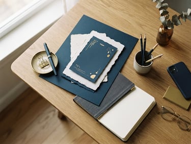 Overhead view of a minimalist workspace, warm editorial photography, soft side-lit window light, deep navy and muted gold tones, tactile paper mockups, 35mm