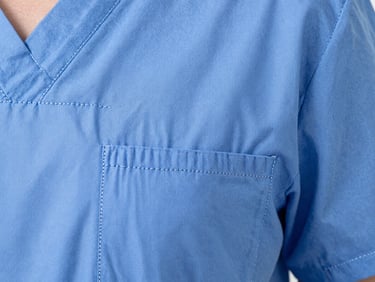 Macro shot of reinforced double-stitching on a medical scrub pocket, showing the tight, precise seams. Bright clinical studio light, sharp focus.