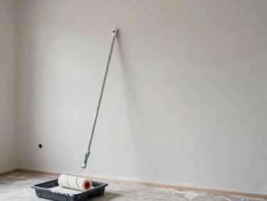 Wide shot of a freshly painted interior wall in a light neutral tone, paint roller resting on a tray in the foreground, bright ambient daylight, no people visible